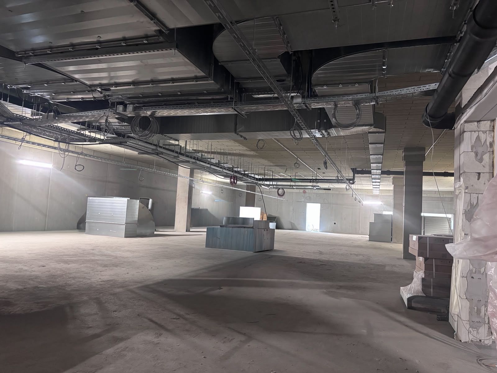 Üres ipari csarnok beton mennyezete alatt szerelt fő gerinc légcsatorna, függesztett kábeltekercsekkel és szerelvényekkel